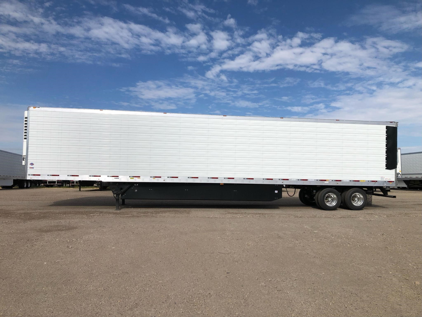 Trailer side view showing a long white refrigerated trailer with black undercarriage and wheels.