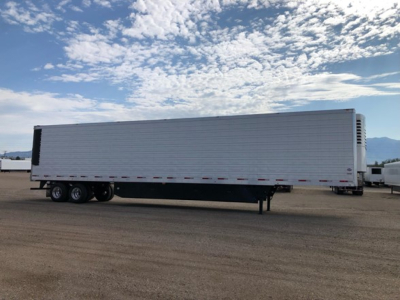 Trailer with a white utility reefer box and black undercarriage. Side text not legible. Flat paved lot under blue sky.