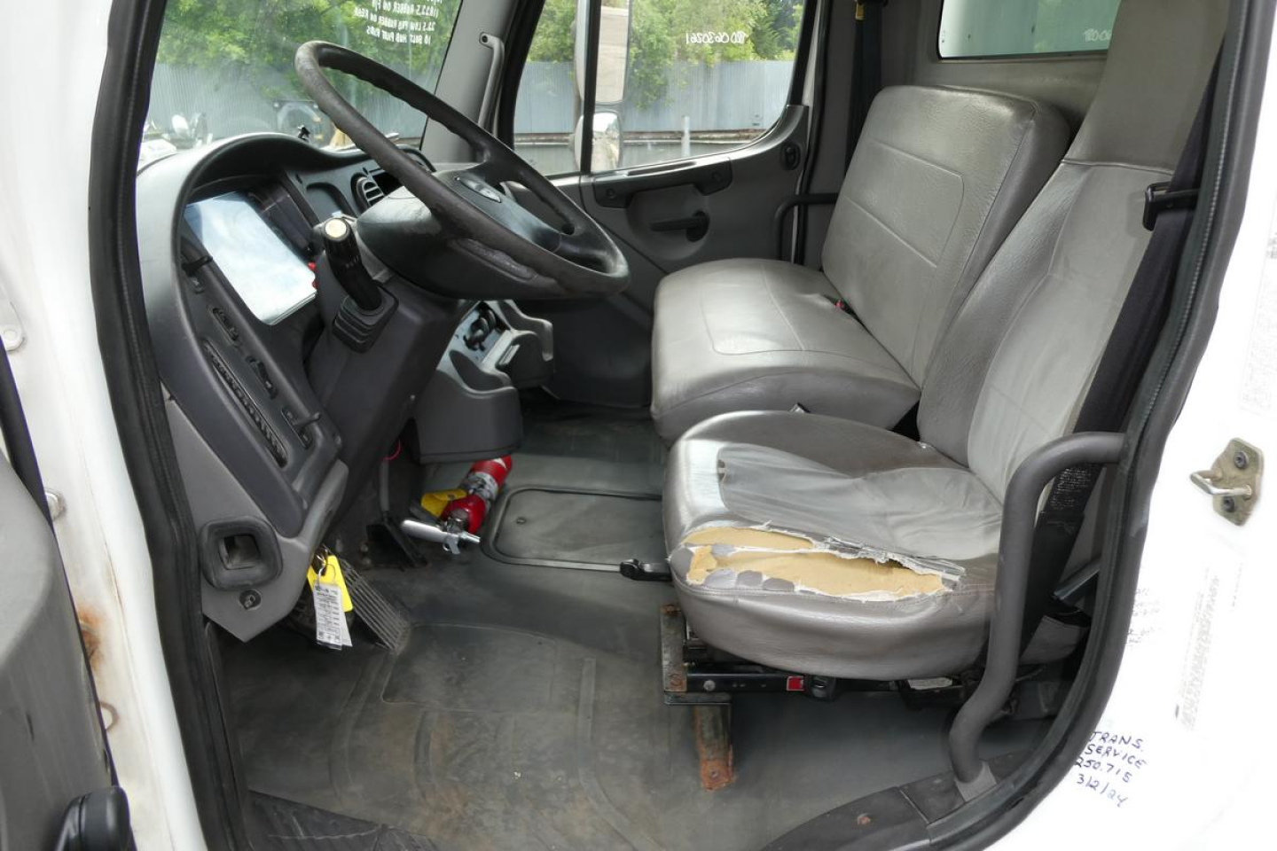 Freightliner M2 106 truck cab interior showing steering wheel, driver seat with torn cover, and dashboard panel.