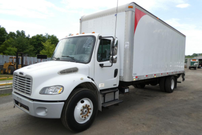 Box truck 2007 Freightliner M2 106 side view with box cargo body and cab, white front, gray bumper, parked in yard.