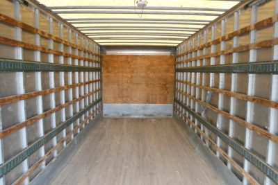 Truck box interior showing empty cargo area with wooden side rails and metal floor, light from rear.