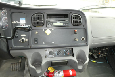 Dashboard view of Freightliner M2 106 interior with radio, HVAC controls, steering column, ignition, and fire extinguisher visible under dash.