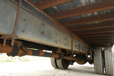 Underbody view of a Freightliner M2 106 box truck showing frame rails, suspensions, and dual rear wheels with rust-colored components.