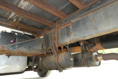 Underbody view of Freightliner M2 106 showing chassis, drive shaft, and suspension components with visible rusted brackets and fuel tank.