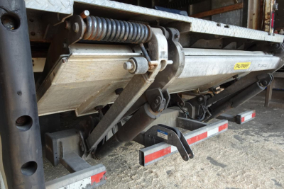 Freightliner M2 106 undercarriage showing hydraulic lift mechanism and metal rail with label, parts of a flatbed or box truck chassis.