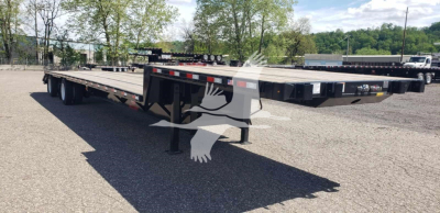Flatbed trailer with beavertail section in a parking lot. No visible text on the trailer; the image shows a long lowbed/flatbed trailer with multiple axles and a black frame.