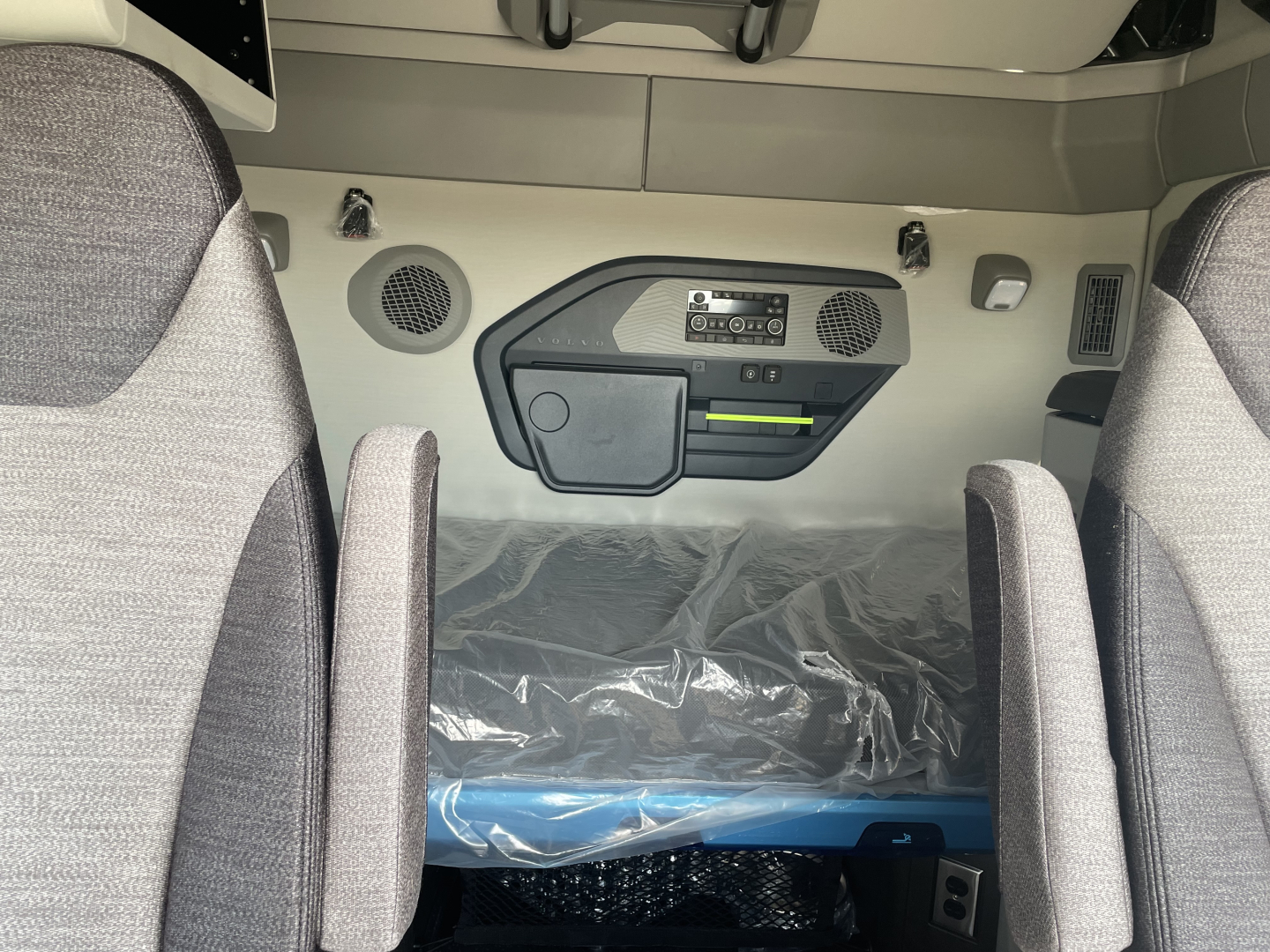 Rear sleeper area of a Volvo VNL truck showing overhead console and control panel, with two seats and a plastic-covered sleeping area.