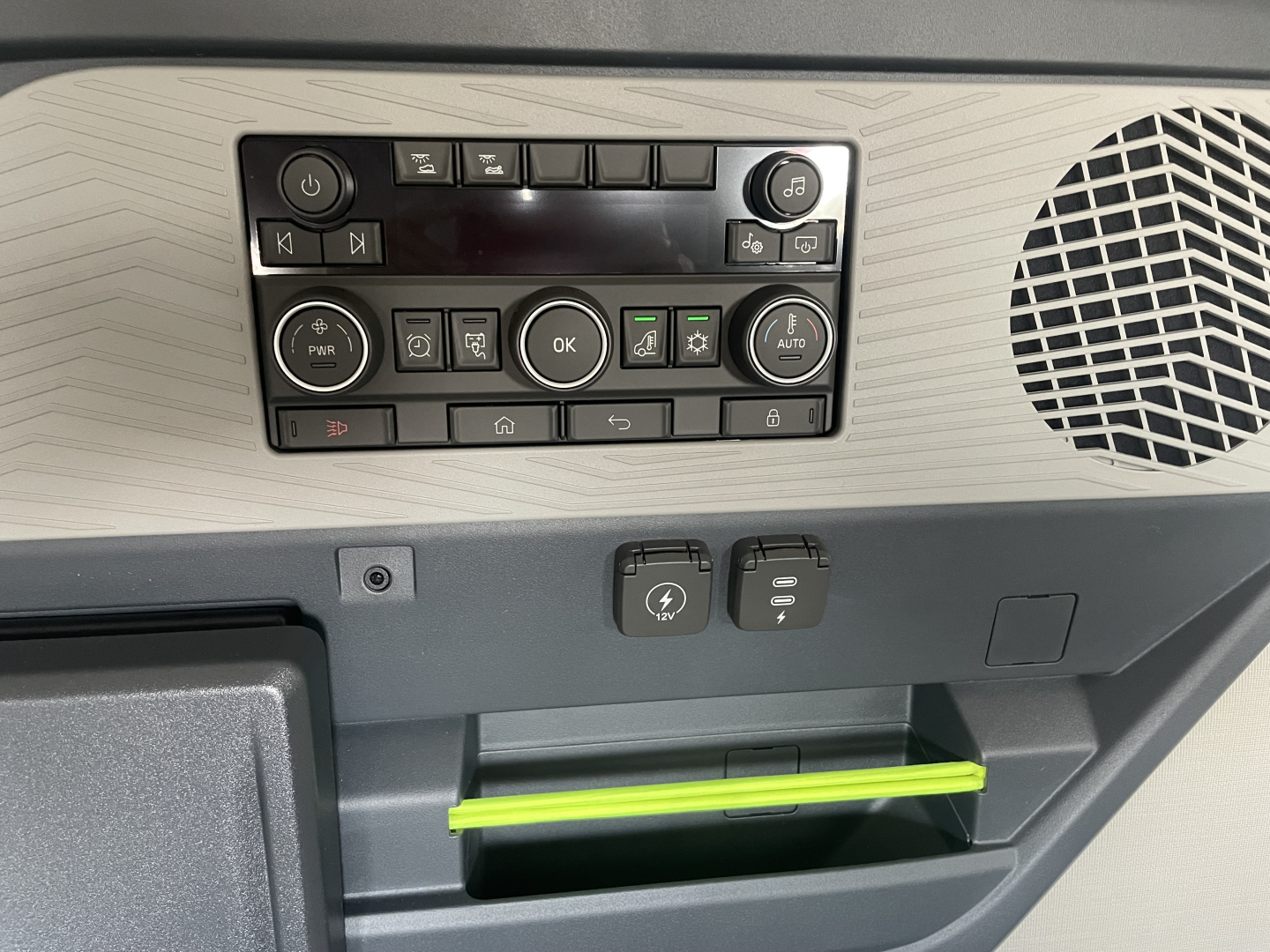Dashboard controls and storage area in Volvo VNL64T660 cabin showing control panel with numerous buttons, speaker grill on right, and a lime green tray handle.