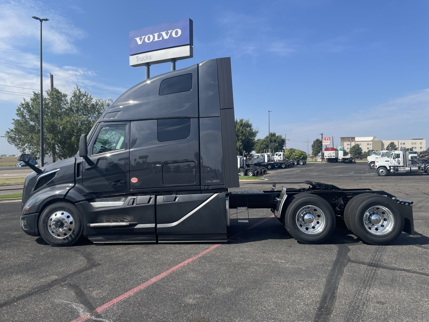 Volvo VNL64T660 tractor unit in black, side view showing sleeper cab and dual rear axles, with Volvo Trucks sign in background.