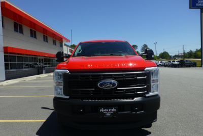 Ford pickup truck front view showing large black grille with Ford emblem, red hood and sides, black bumper; dealership plate frame reads Peach State Ford.