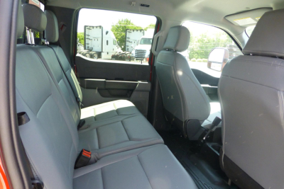 Truck interior showing rear bench seat and front seats with light gray upholstery; rear doors open; view toward front passenger area; minimal dashboard controls visible.