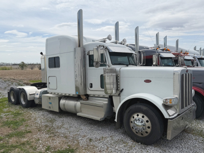 Peterbilt 389 UltraCab tag in a used truck lot showing a white conventional sleeper tractor with chrome exhaust stacks and dual rear axles.