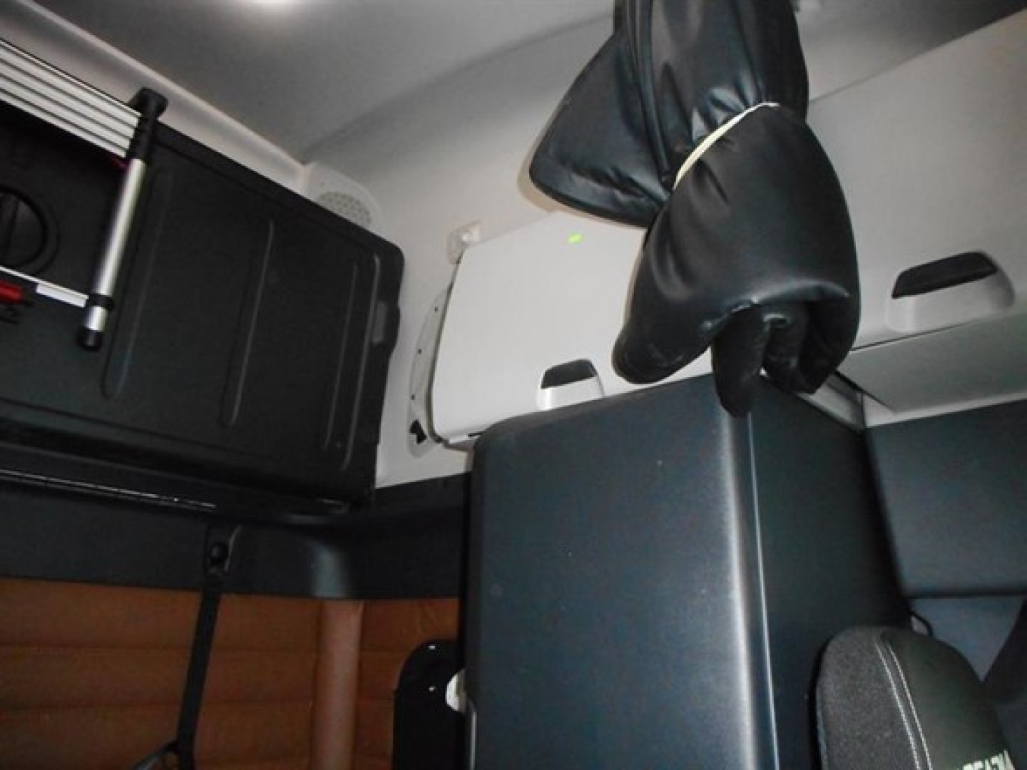 Cab interior of a Freightliner Cascadia 126 sleeper showing storage compartments and a seat with upholstery and overhead components.