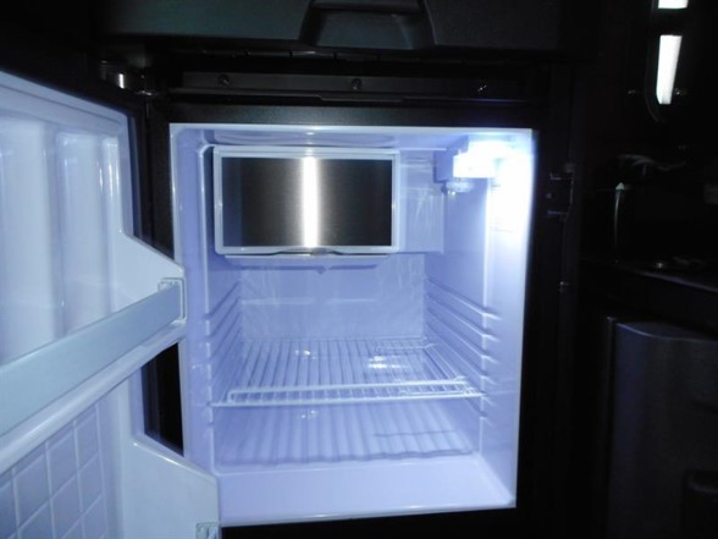 Freightliner Cascadia 126 truck sleeper interior showing empty refrigerator/minibar unit and open upper cabinet with bright interior light.