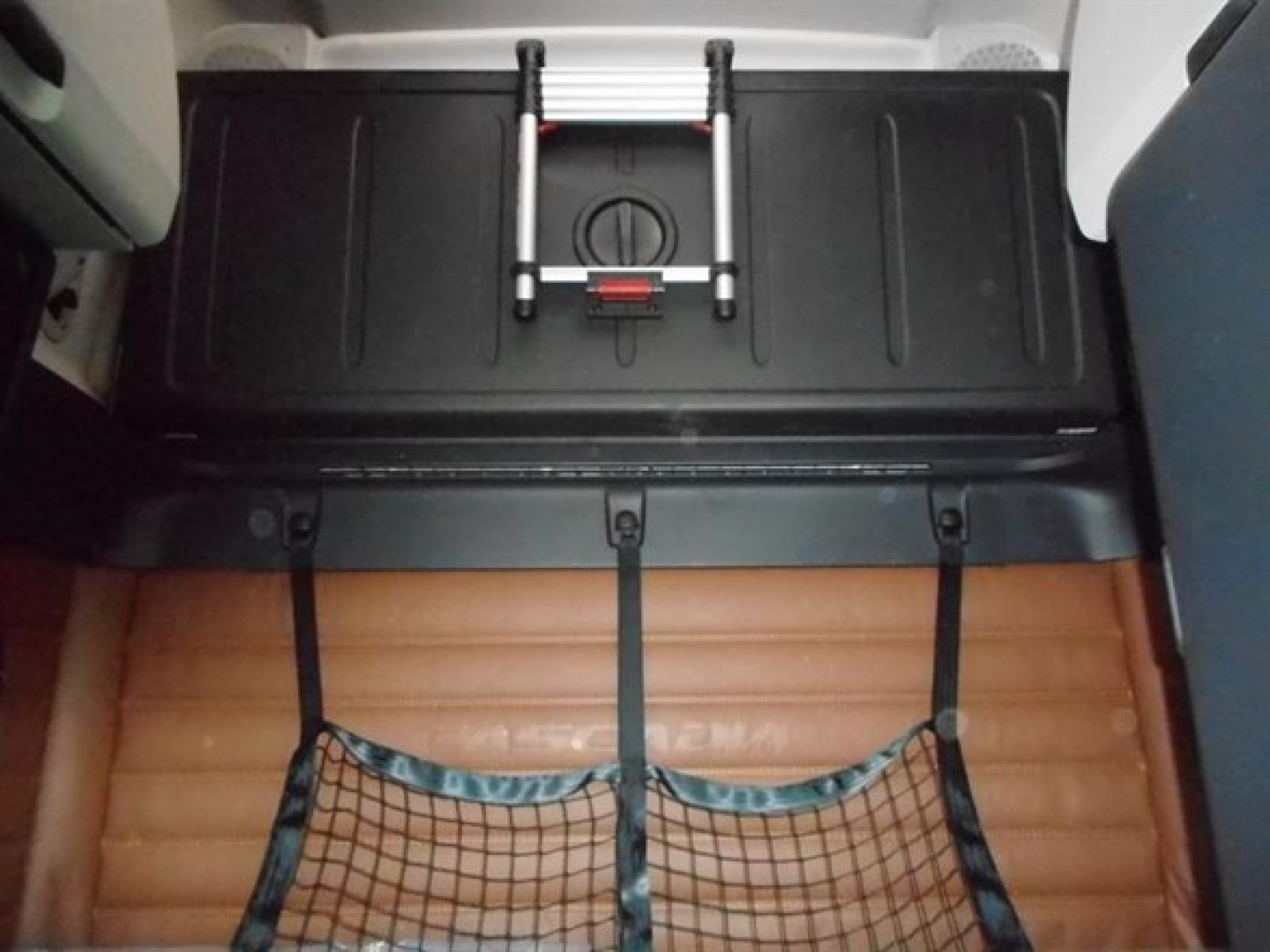 Freightliner Cascadia cab interior with rear storage hatch and brown sleeper mattress visible.