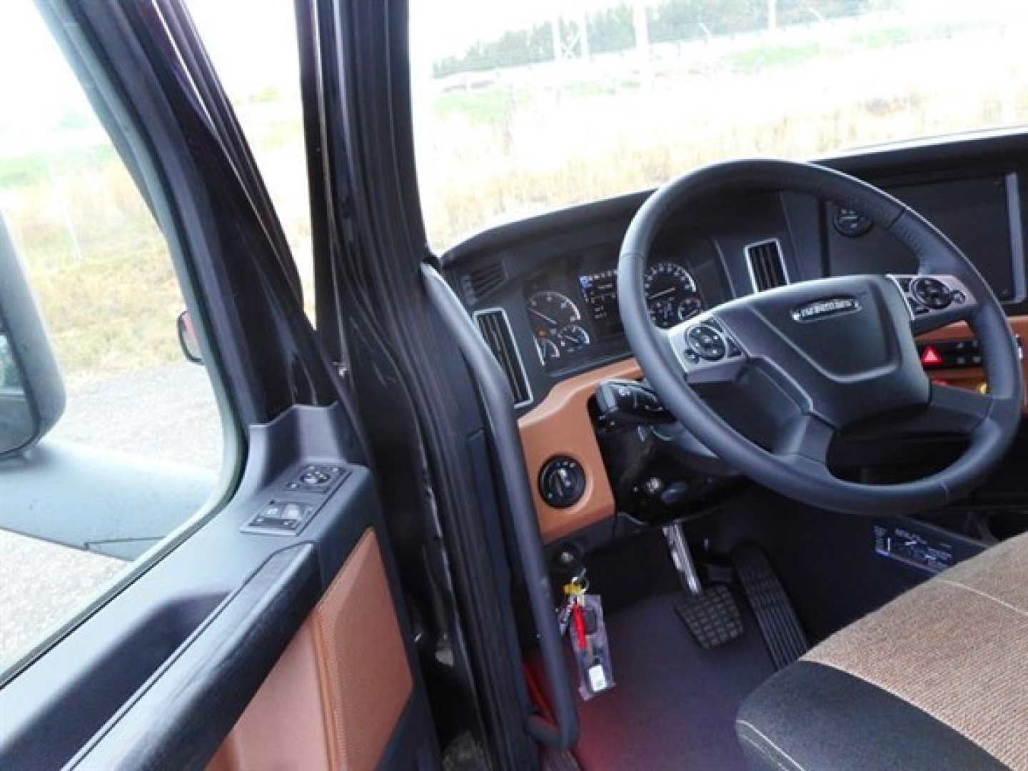 Truck interior showing steering wheel, dashboard, and driver's seat with visible controls and keys hanging from ignition.