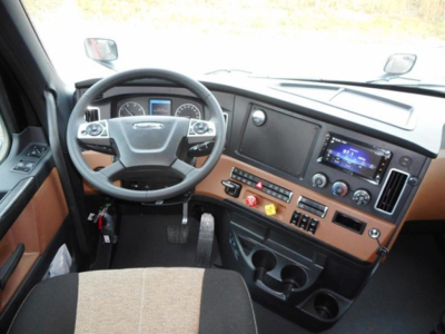 Truck cab interior showing steering wheel, dashboard with touchscreen, and control panel.