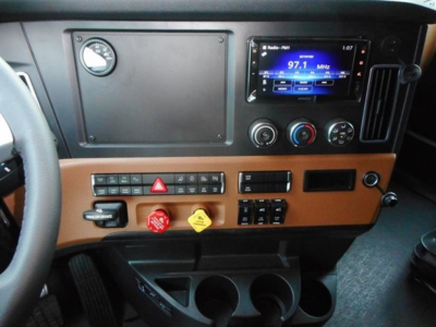 Dashboard of new 2027 Freightliner Cascadia 126 sleeper with tan dashboard, digital radio display, climate controls, switches, and cup holders.