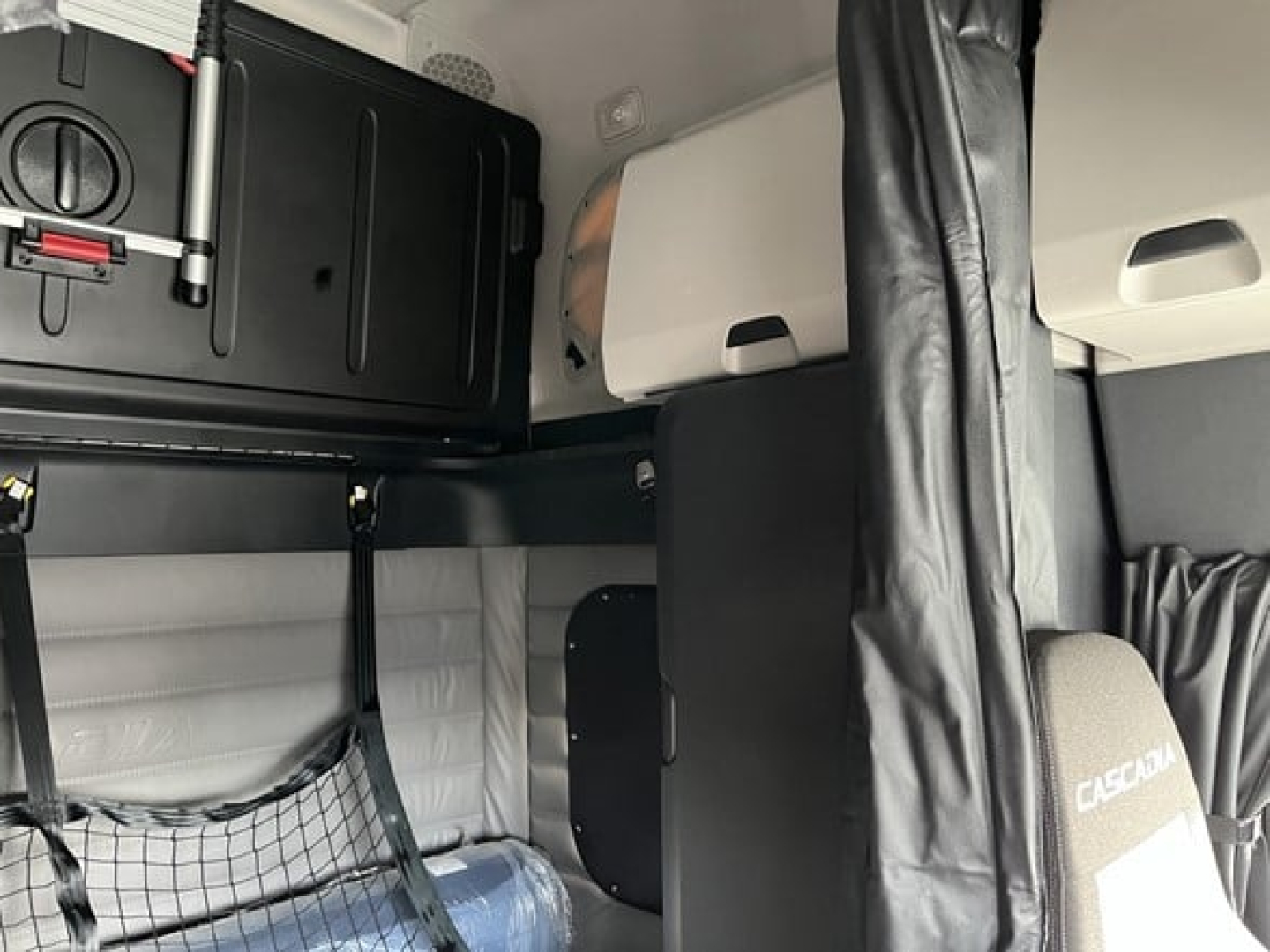 Freightliner Cascadia 126 cab interior showing sleeper area with storage cabinet, black equipment box, and fabric seating.