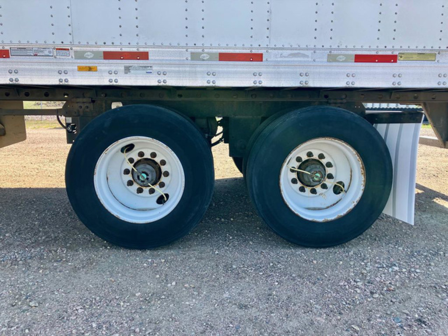 Dual rear wheels of a utility van trailer showing white rims with black tires and undercarriage components.