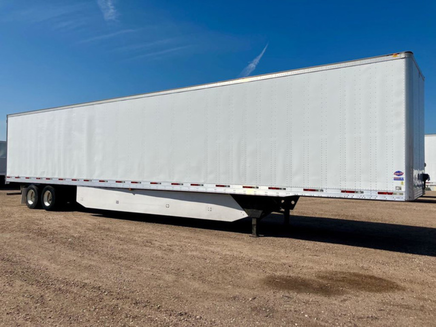 Trailer semi-trailer box on a white chassis and parked on dirt lot, used condition.