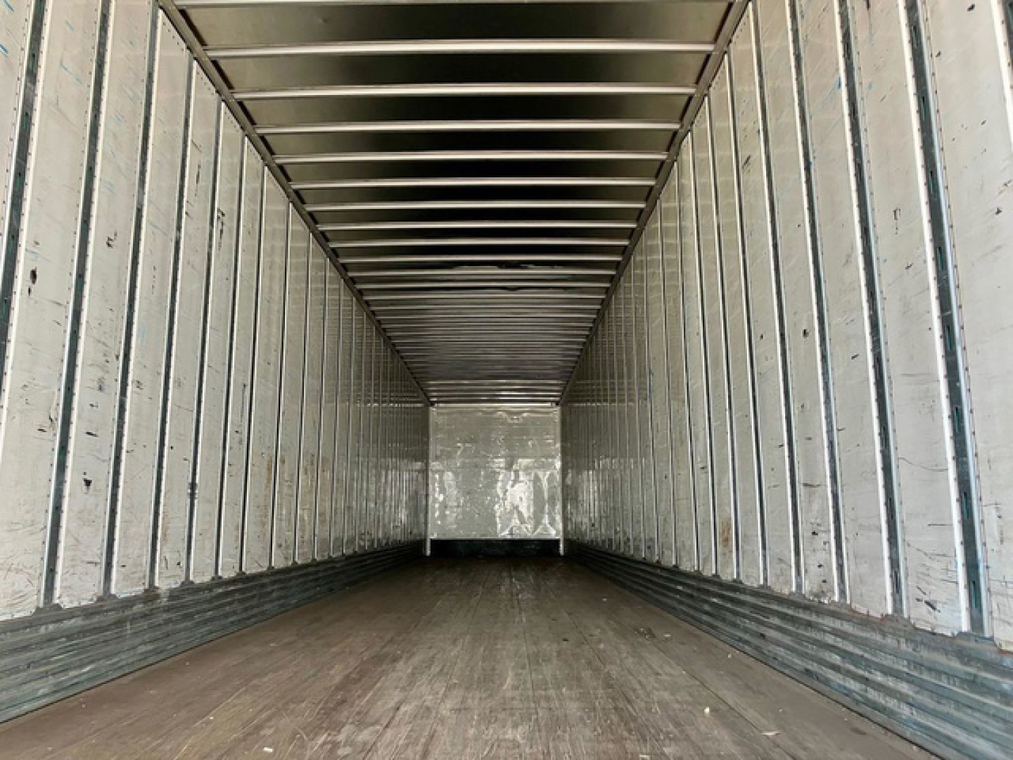 Trailer interior showing empty metal cargo area with ribbed walls and wooden floor, long rectangular van-like trailer