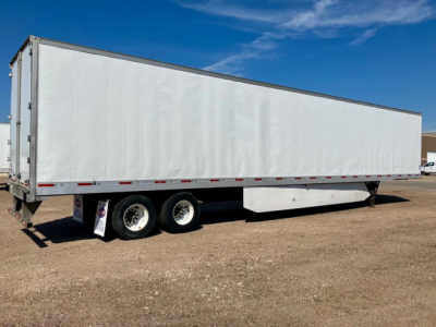 Trailer shows a long white utility dry van with dual rear axles and trailer side skirts, under a clear sky.