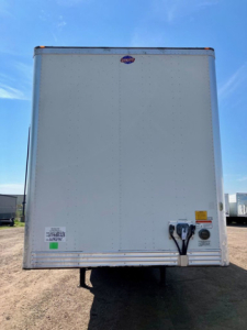 Rear view of a box trailer with a clean white surface, back doors closed, visible hitch and electrical connections, no text clearly legible except small stickers.