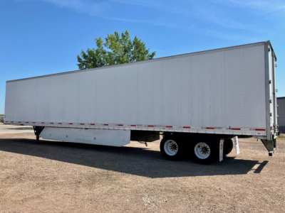 Trailer side view showing a large gray box trailer with double rear axles and a raised landing gear, no visible branding.