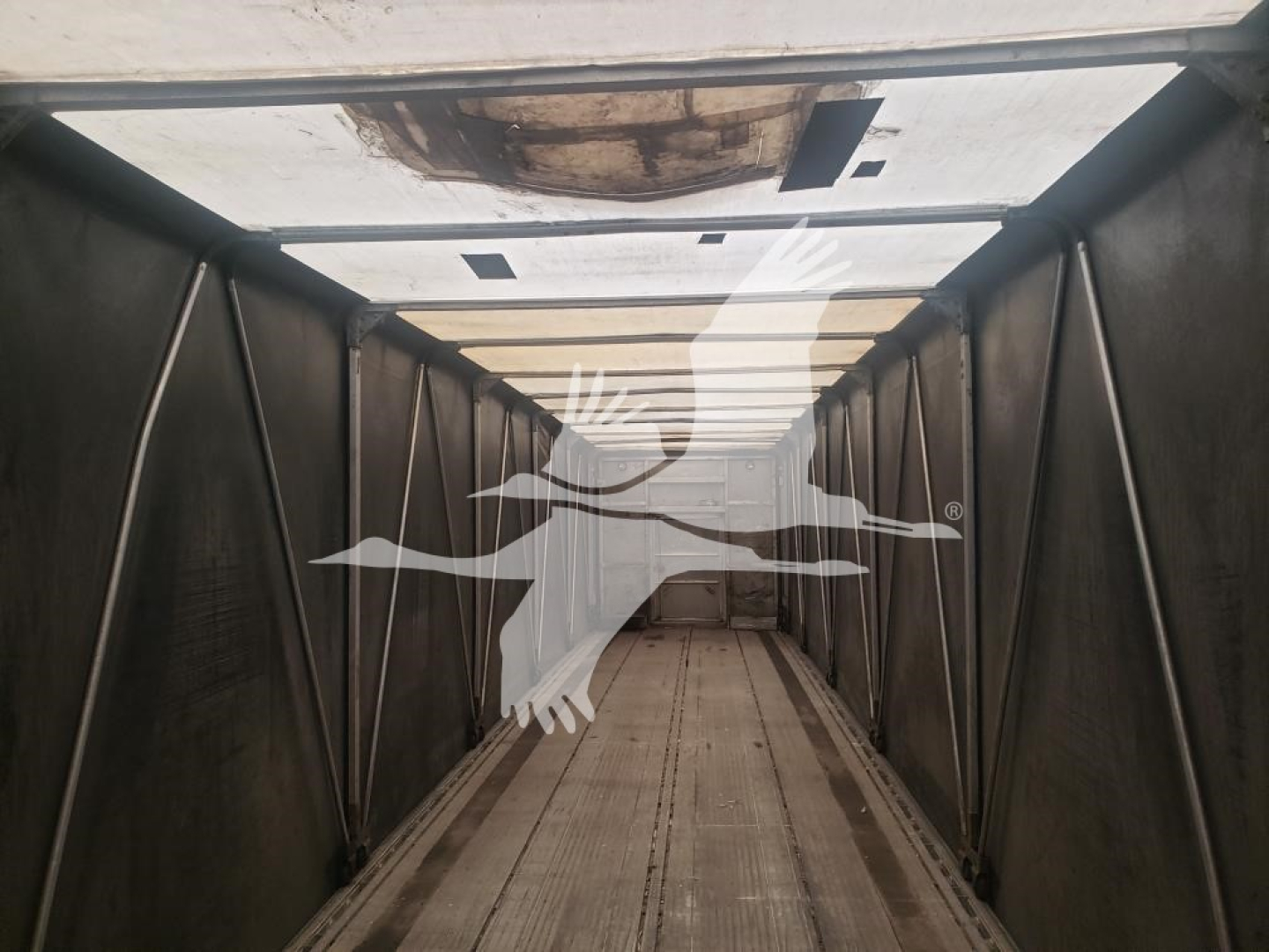 Trailer interior showing a long flatbed trailer withCurtainside design, empty cargo area, light panels along the ceiling.