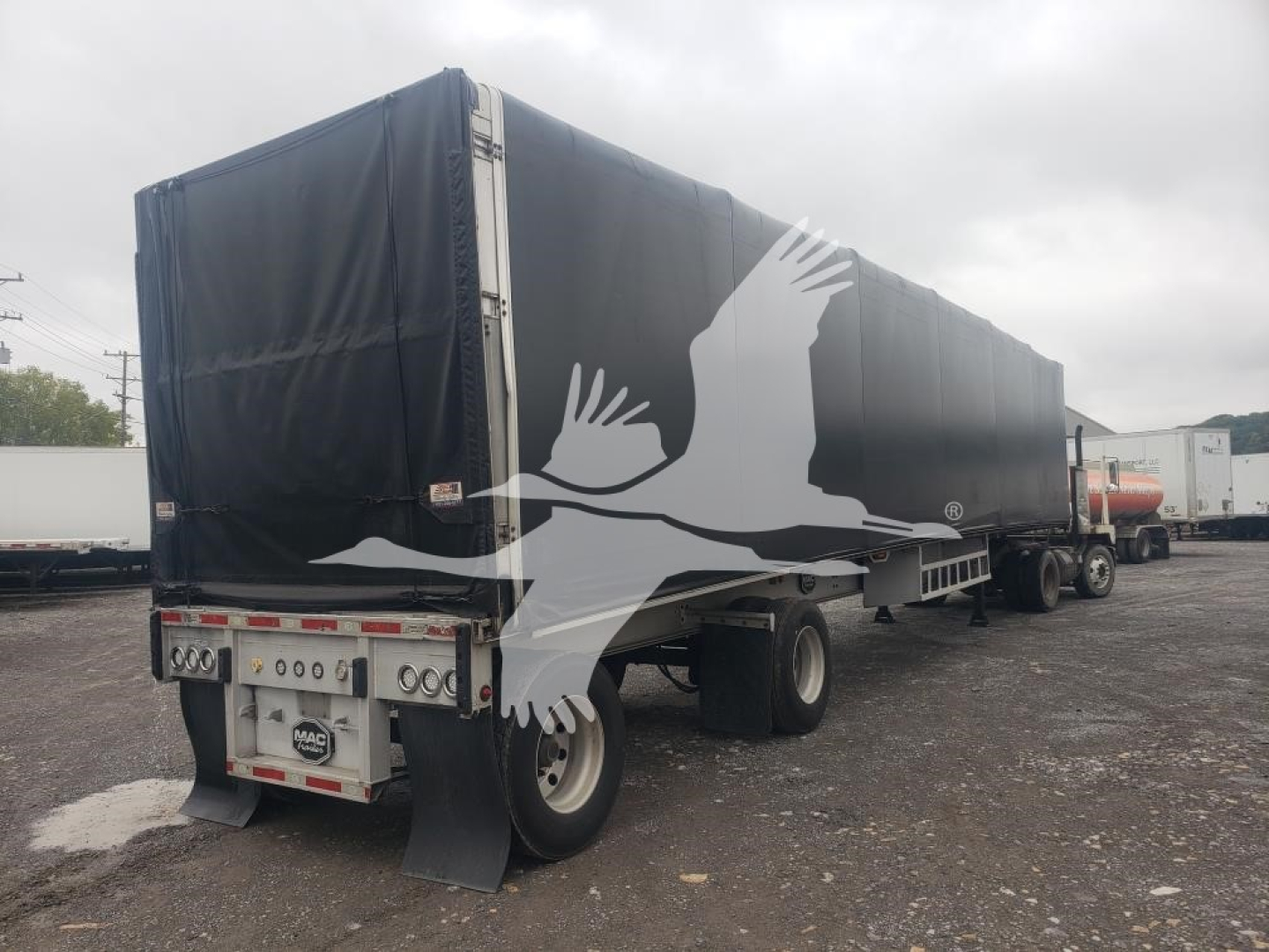 2015 Mac flatbed curtain-side trailer with black tarp sides and large white eagle graphic on side. Rear shows MAE/CARGO TRAILER branding and taillights. Flatbed dual axles with black mud flaps, overcast lot.