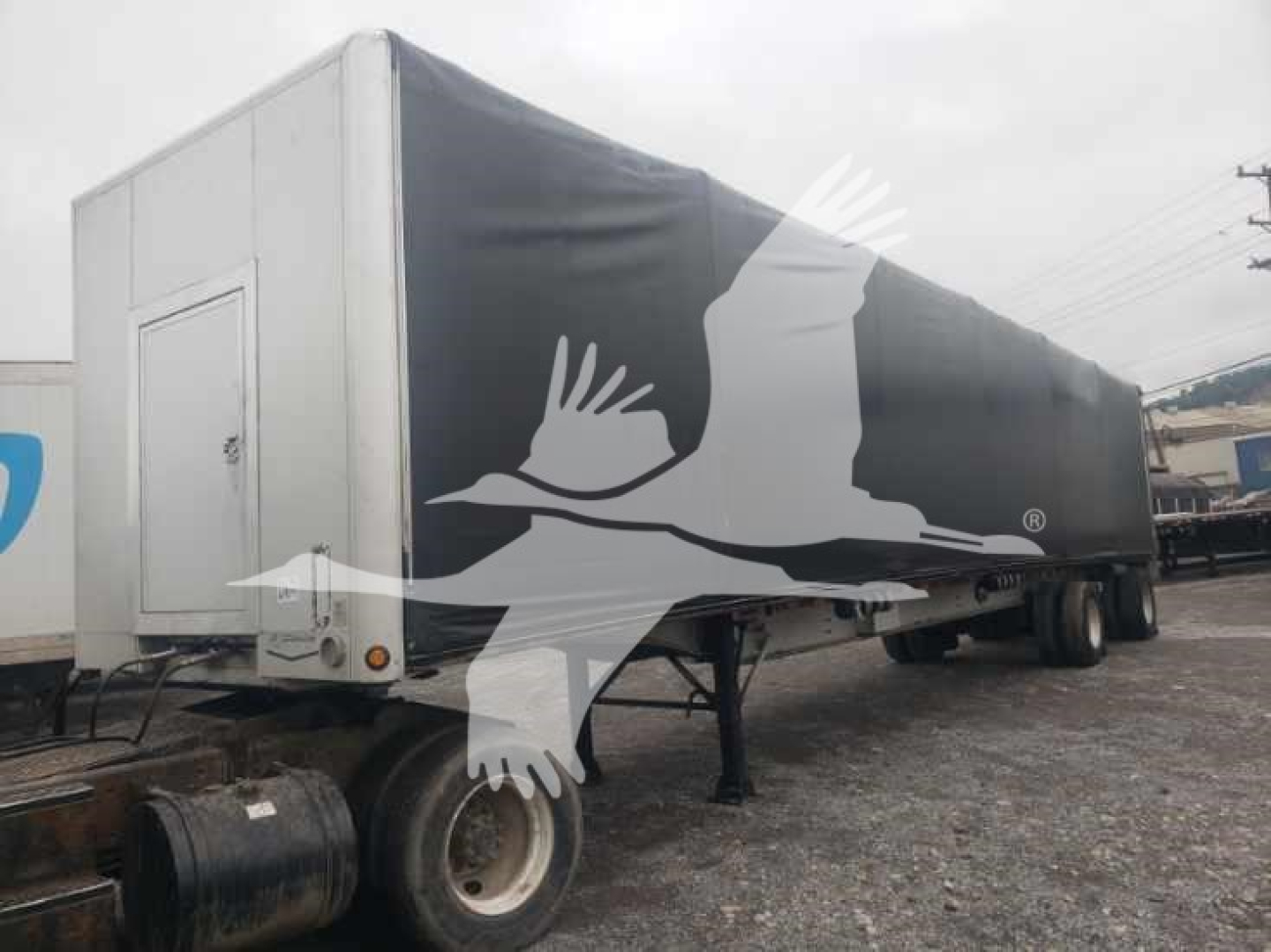 Trailer side view showing curtainside flatbed with black cover and white graphics, front neck area with landing gear and wheels.