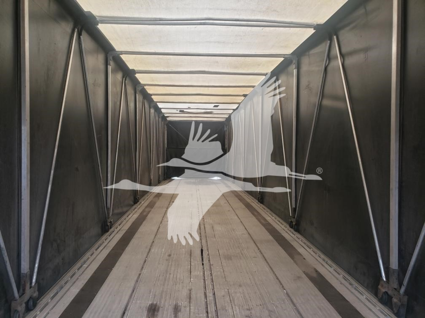 Trailer interior showing curtainside Mac flatbed with metallic side walls and wooden deck under bright light