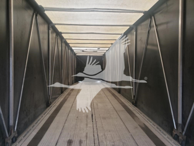 Trailer interior showing curtainside Mac flatbed with metallic side walls and wooden deck under bright light