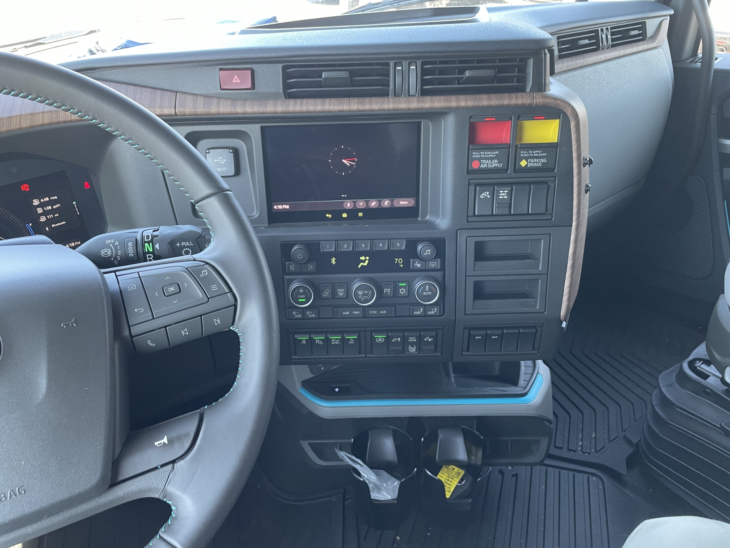 Volvo VNL64T860 dash and center console showing touchscreen display, climate controls, and auxiliary switches in cab View with steering wheel and pedal area visible