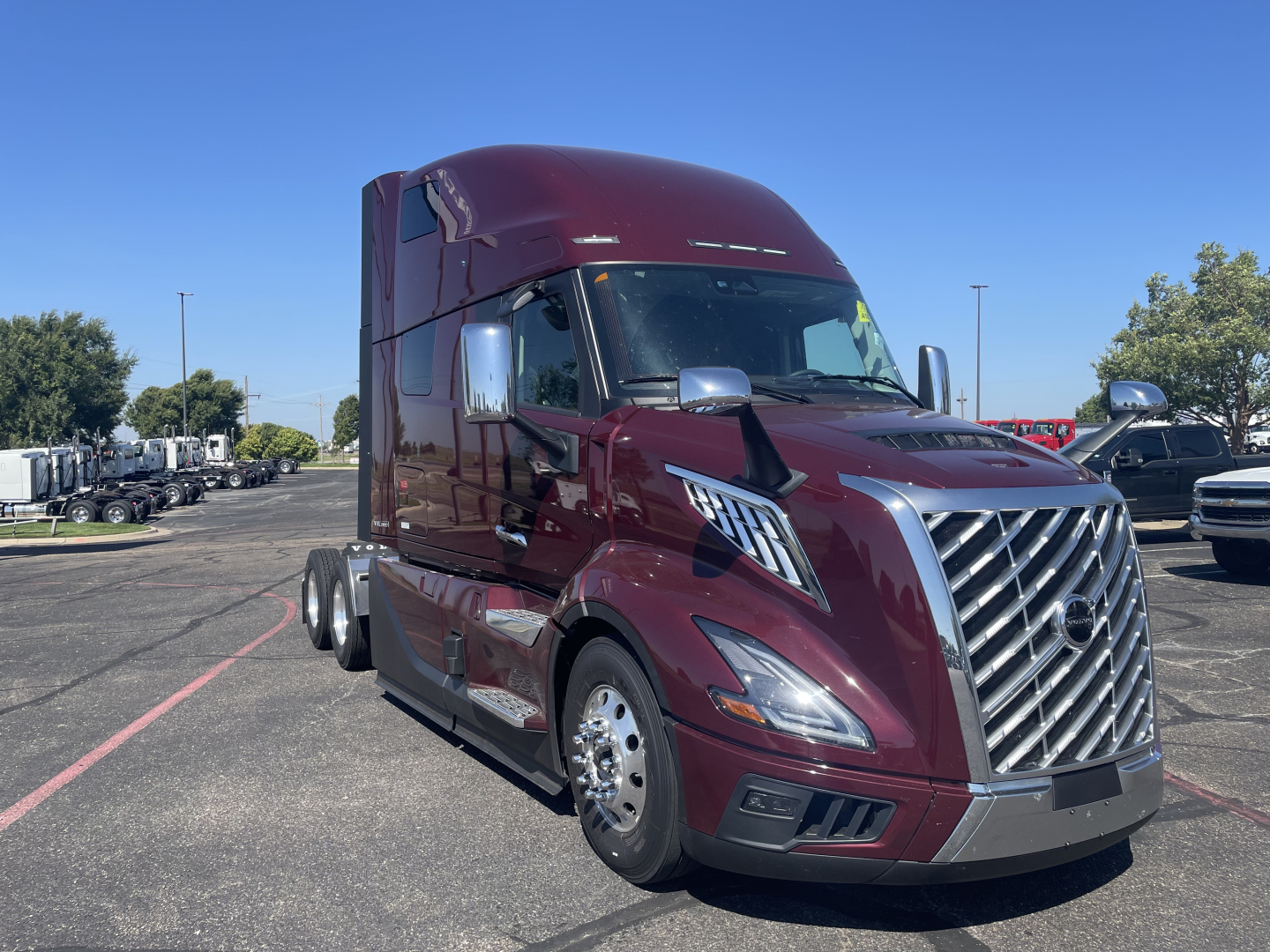 Volvo VNL64T860 truck in maroon showing front grille, headlights, and side mirror; sleeper cab with chrome accents and large aerodynamic bumper.