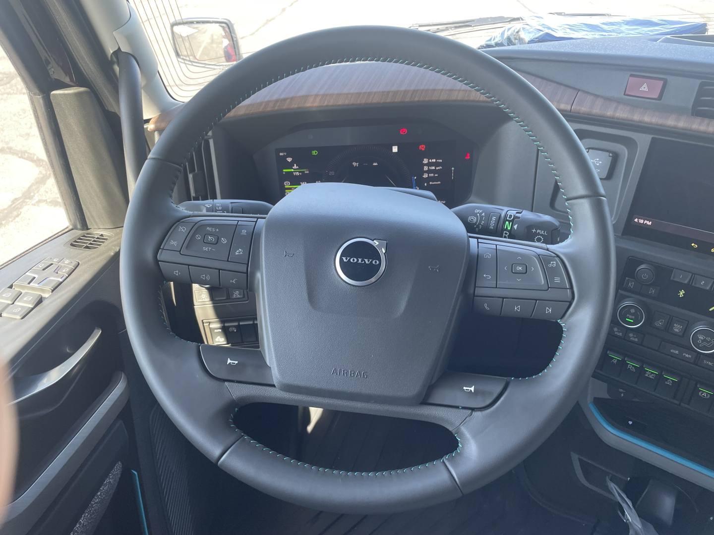 Volvo truck steering wheel and dashboard with Volvo logo center, digital instrument cluster visible.