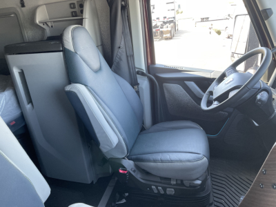 Volvo VNL cabin front interior showing driver seat and steering wheel with dashboard, light gray upholstery, and visibility of sleeper area.
