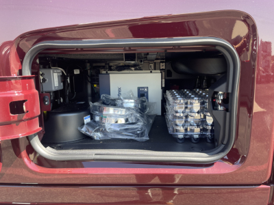 Volvo engine bay view showing storage area with packaged components and stacked battery packs.