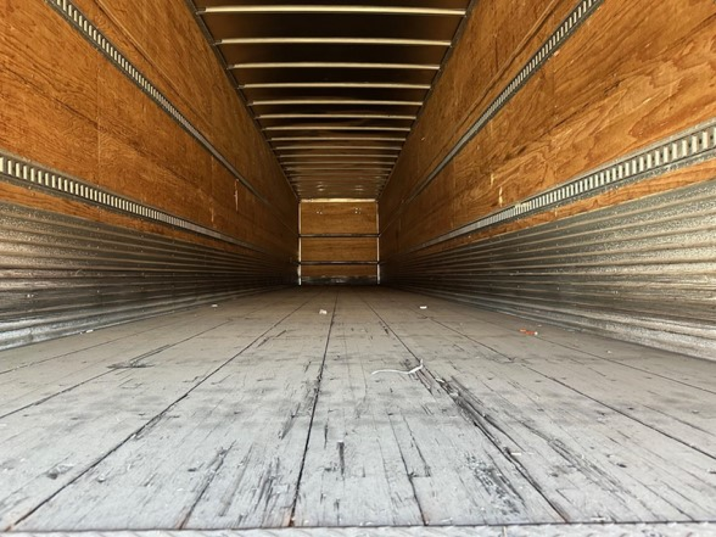Trailer interior showing wooden sidewalls and metal cargo rails with worn flooring in a dry van.