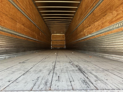 Trailer interior showing wooden sidewalls and metal cargo rails with worn flooring in a dry van.