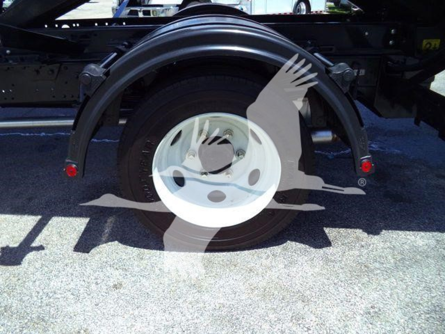 Truck rear wheel and fender of a 2024 Isuzu NPRR rolloff truck showing white steel wheel and black frame with red reflectors