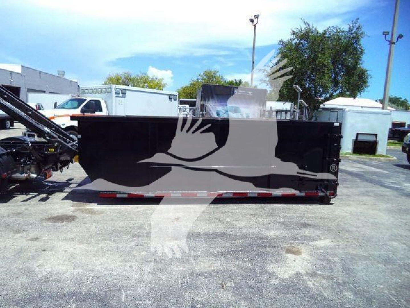 Isuzu NRR rolloff truck body side view showing solid black cargo bed with reflective safety markings and background equipment.
