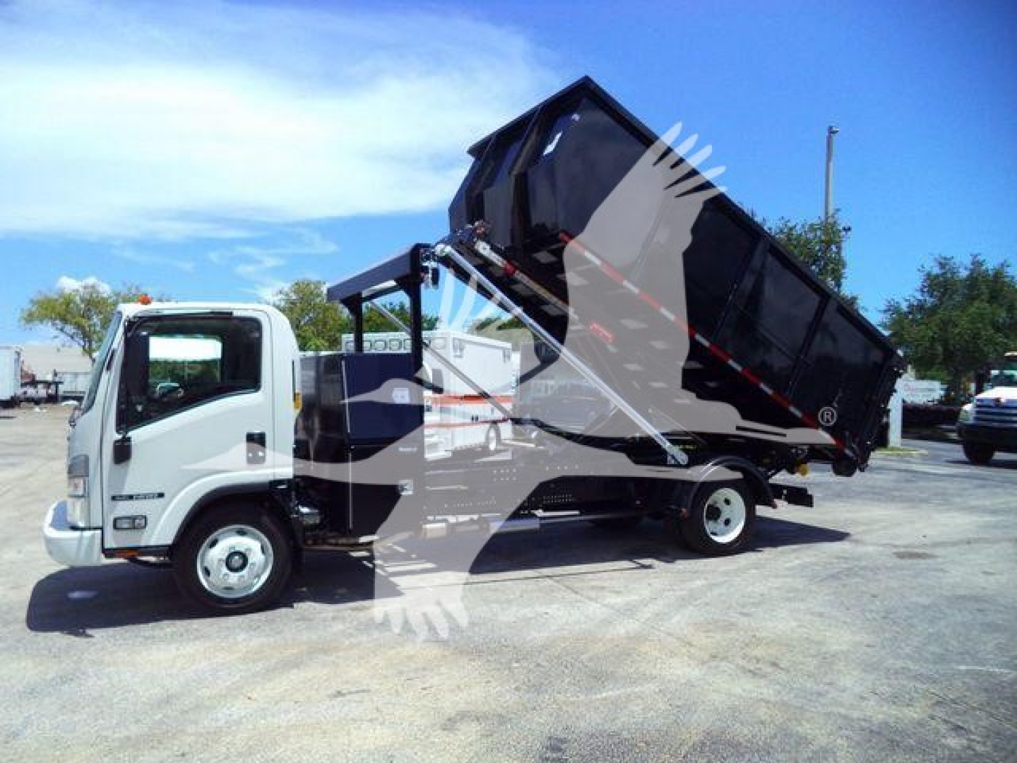 Isuzu NPR/NRR dump truck with a raised black dump bed. Vehicle side view showing cab, front wheel, and hydraulic tipping mechanism.