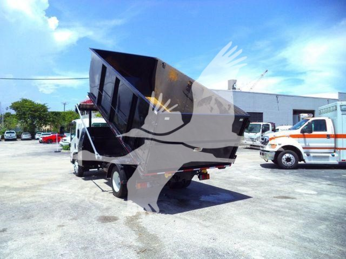 Isuzu NPRR roll-off truck with raised dump bed in a dealership lot.
