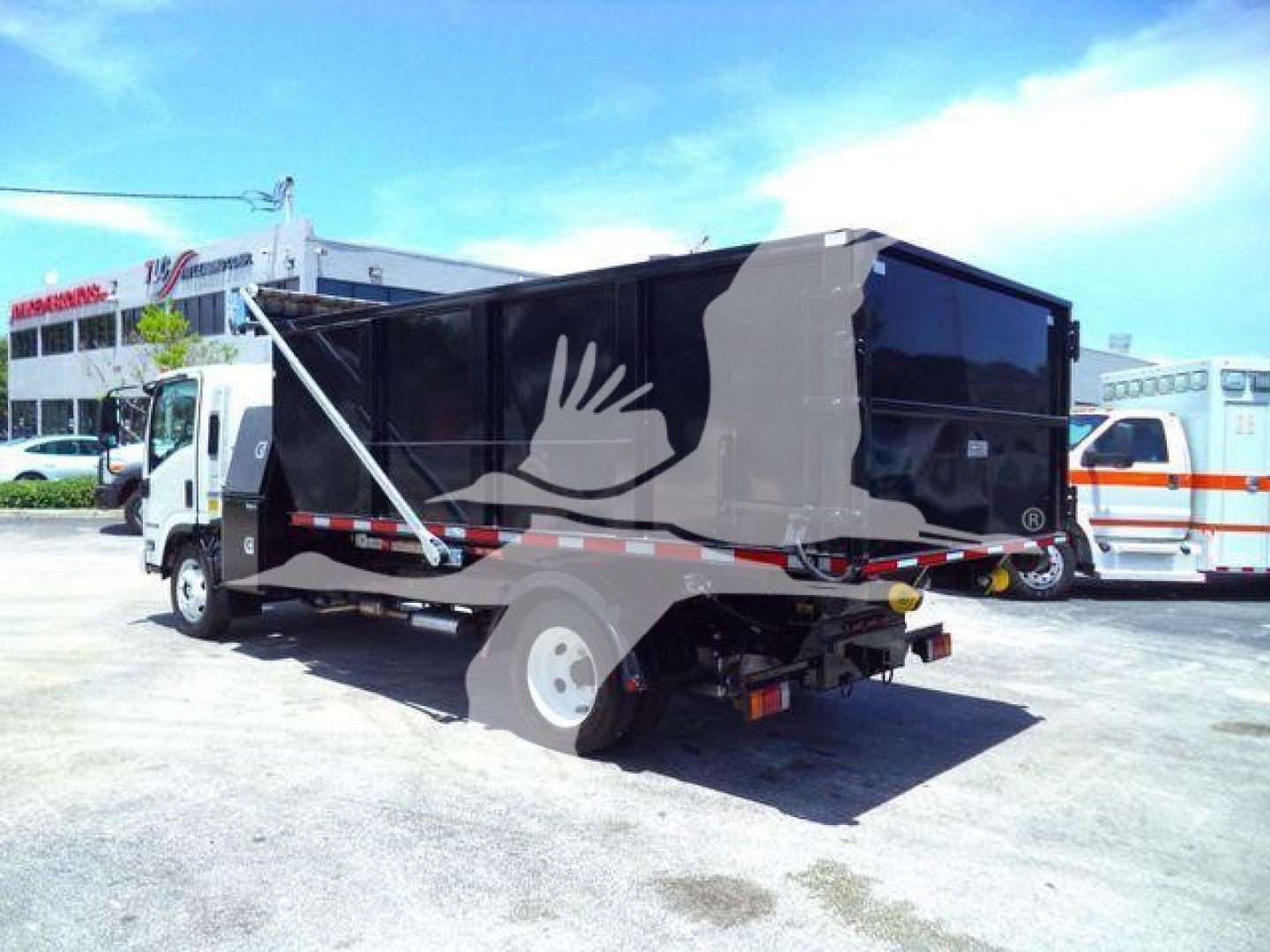 Isuzu NRR roll-off truck in a parking lot, black dump body with white wheels and rear view showing hydraulic mechanisms and side panel; stock and category not visible in image