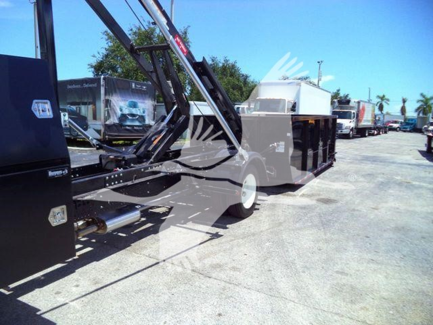 Isuzu NRR roll-off truck in a dealership lot showing hydraulic crane and waste container body.