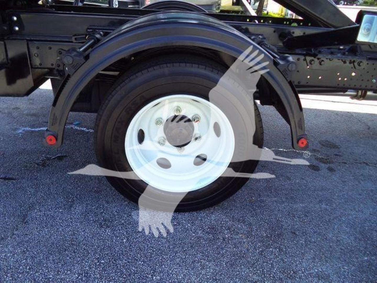 Isuzu NRR wheel and fender view showing white steel wheel and black tire on a roll-off truck chassis.