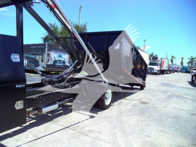 Isuzu roll-off truck body with hydraulic arms and dump bed, side view showing blue sky and other trucks in lot.