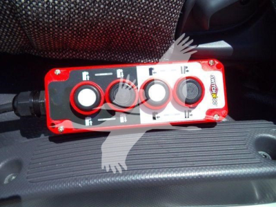 Red control panel with four circular knobs labeled with white icons on a truck interior surface.